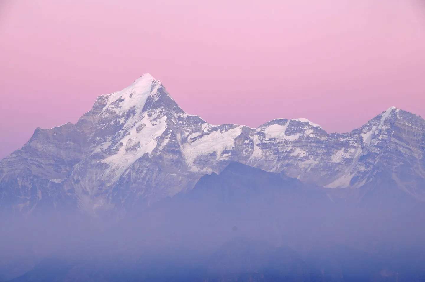Dunagiri, as the photographer's file title identifies it, seen from Kuari Pass in the early morning: a steep pyramid with a lower summit to its right, pale snow and rock under a pink sky, with blue-violet mist filling the valleys below.
